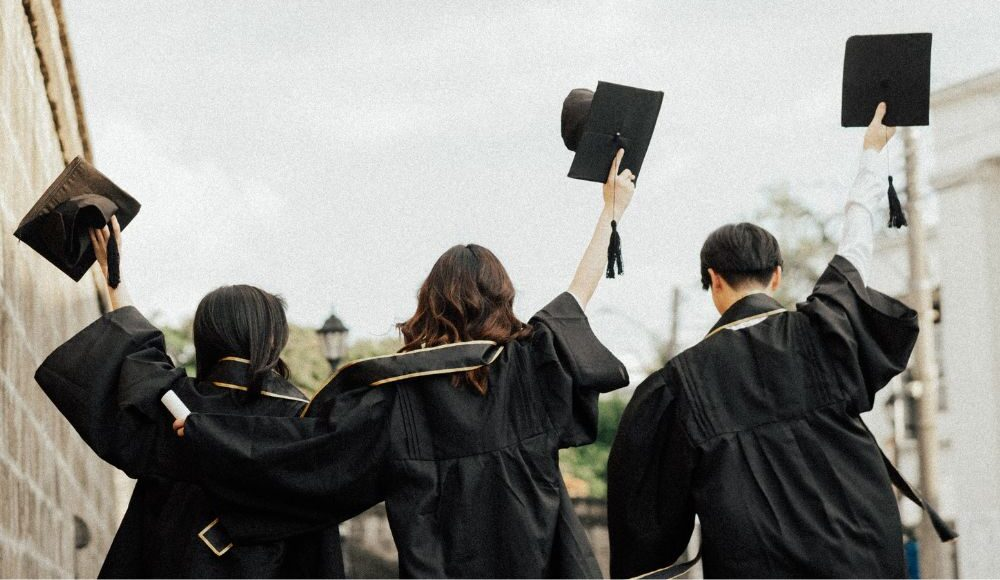 Three students hold up their caps wearing graduation gowns